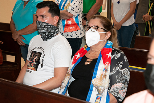 Con una camiseta con lema mariano y un pañuelo con imágenes de la Virgen de la Caridad y la bandera cubana, dos fieles participan en la Misa por Cuba celebrada por el Arzobispo Thomas Wenski el 13 de julio de 2021 en la Ermita de la Caridad en Miami.