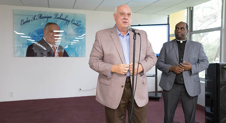 Carlos Manrique, director of school operations in the Division of Adult & Workforce Education for Miami Dade County Public Schools, speaks at the July 21, 2021 blessing and ribbon-cutting of a new community computer literacy center at Notre Dame d'Haiti Mission in Miami. which is named after him. At right is Notre Dame d'Haiti's administrator, Father Reginald Jean-Pierre.