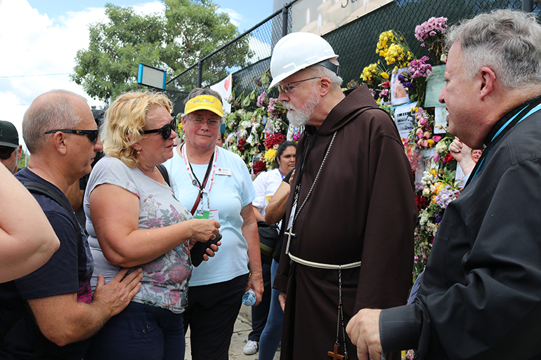 Boston Cardinal Sean Patrick O’Malley speaks with the mother of Anastacia Gramova, one of those missing in the collapse of the Champlain Towers South condominium in Surfside, during a July 2, 2021 visit to the memorial wall located near the collapse site. At center is Martha Lohrstorfer, a volunteer counselor with the Red Cross.