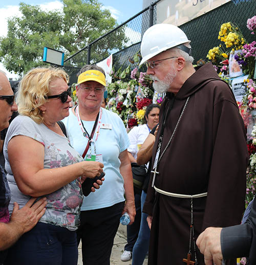 Martha Lohrstorfer, voluntaria de la Cruz Roja  Americana y católica de Michigan (centro), escucha mientras una mujer que busca a su hija desaparecida habla con el Cardenal de Boston Sean O'Malley, durante su visita al lugar del derrumbe de Champlain Towers South, el 2 de julio de 2021.