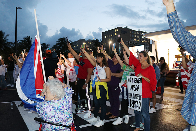 Dozens of Cubans living in the diaspora, who gathered at the National Shrine of Our Lady of Charity in Miami July 14, 2021, to pray for their homeland, raise their cellphones, with their flashlights on, while facing across Biscayne Bay toward the island.