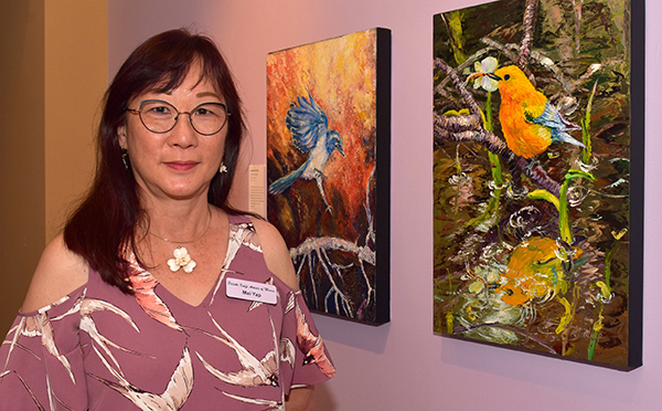 MaiYap, founder of the Palette Knife Artists of Miami, shows Lorraine Tucker's painting of a Florida scrub jay, left, and her picture of a prothonotary warbler.