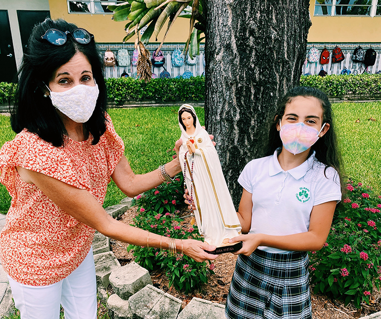 Vanessa Medina, a fifth grade student at St Kevin School, hands her statue of La Virgen Maria Rosa Mystica to Diane Perez-Cubas, intermediate grade level curriculum coordinator and religion teacher.