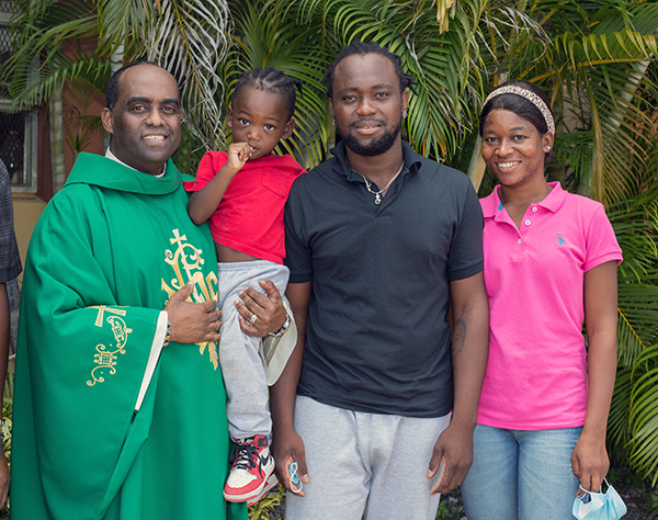 El P. Reginald Jean Mary, párroco de Notre Dame d'Haiti, sostiene a Kevin-Jay Metellus, de 28 meses, mientras posa para una foto con sus padres, Kervens Metellus y Marlene Belizaire, fuera de la iglesia de Notre Dame d'Haiti. Todos ellos llegaron de Texas alrededor de la medianoche del 26 de septiembre de 2021.