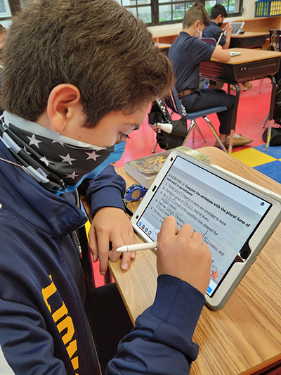 A middle school student from St. Mark School works on an English lesson from his iPad.