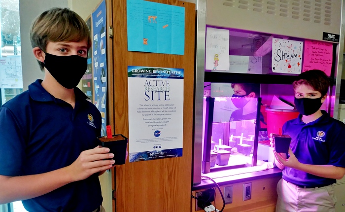 Mary Help of Christians students Philip Sampson and Emmanuel Segui place newly planted radish seeds into a growth chamber.