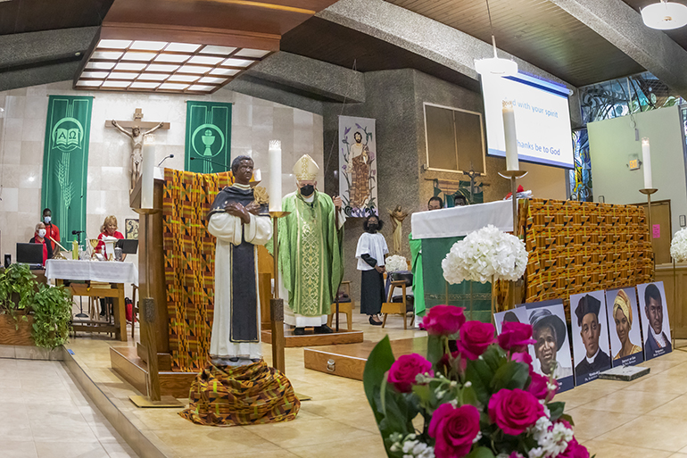 Surrounded by images of black saints and saint-in-waiting, Archbishop Thomas Wenski celebrates the Mass for Black Catholic History Month at St. Bartholomew Church in Miramar, Nov. 6, 2021. The images include a statue of St. Martin de Porres, portraits honoring Black Catholics on the road to sainthood, and an image of the Black Madonna with child.