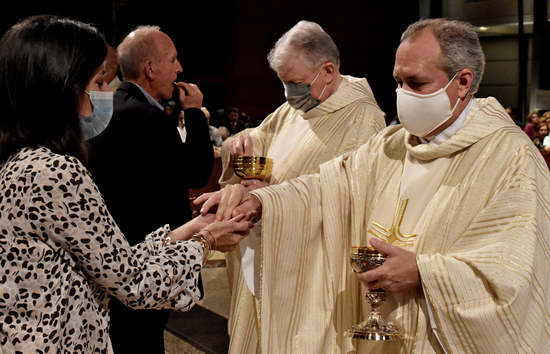 Father Jose Alvarez, foreground, and Msgr. Jude O'Doherty distribute  Communion with a worshiper during the 70th anniversary Mass at Epiphany Church, South Miami, Nov. 20, 2021.