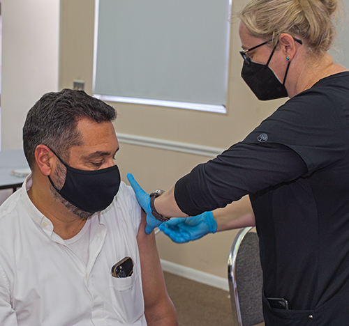 El P. Robert Ayala, párroco de la iglesia St. Matthew, recibe su vacuna de refuerzo de COVID-19 de Raluca Opris Danut, una técnica de farmacia de Walmart, durante la cuarta Feria Anual de la Salud de la parroquia, el 21 de noviembre de 2021.