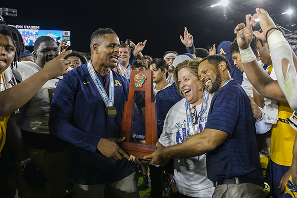 St. Thomas Aquinas head coach Roger Harriott, right, receives the Class 7A State championship trophy from  school principal Denise Aloma and athletic director Twan Russell. Aquinas defeated Tampa Bay Tech, 42-14 at DRV PNK Stadium in Fort Lauderdale, Dec. 17, 2021.