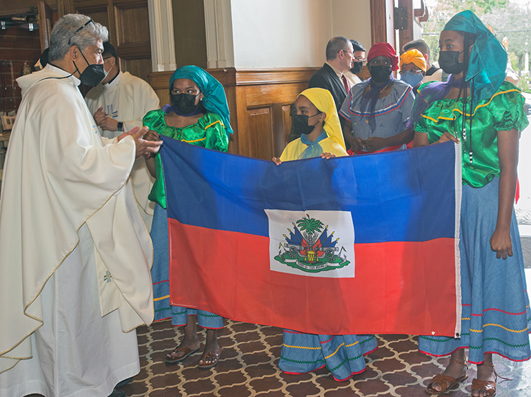 Father Jesus "Jets' Medina, pastor of St. Peter the Fisherman in  Big Pine Key, and archdiocesan director of the Ministry to Cultural Groups, talks to Haitian-Americans Veronica Jackson, 15, Victoria Harris, 9, and Aiyana Michel, 14, as they prepare to enter St. Mary Cathedral with the Haitian flag. Archbishop Thomas Wenski celebrated the annual Migration Mass on the feast of the Baptism of Jesus, Jan. 9, 2022.