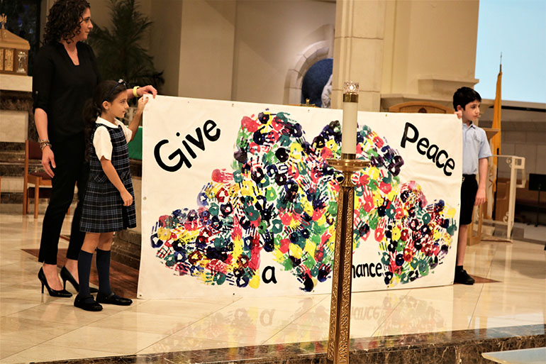 Ella Lurig, 7, and Will Govin, 8, present a piece of artwork at the altar during St. Gregory the Great Parish's evening Prayer Service for World Peace, Feb. 18, 2022. The art was created by students at St. Gregory of the Great School in Plantation where the youngsters attend. Shown with them is Mary Govin, a social studies teacher at the school and mom of Will, who encouraged students to make the banner.
