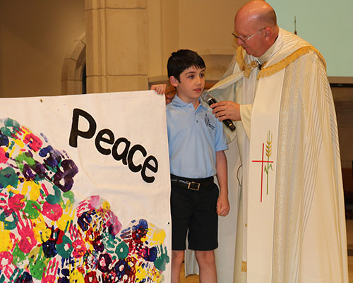 Will Govin, 8, is introduced during Prayer Service for World Peace at St. Gregory the Great Church Feb. 18, 2022. He was one of the students presenting a banner with a message of peace during the evening.