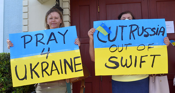 Two women at Assumption of the Blessed Virgin Mary Church, a Ukrainian Catholic congregation in Miami, hold blue-and-yellow signs in the national colors of their homeland Feb. 27, 2022 during the protest against the Russian invasion of that country. The poster at the right refers to the SWIFT international banking system, from which Russia has already been banned.