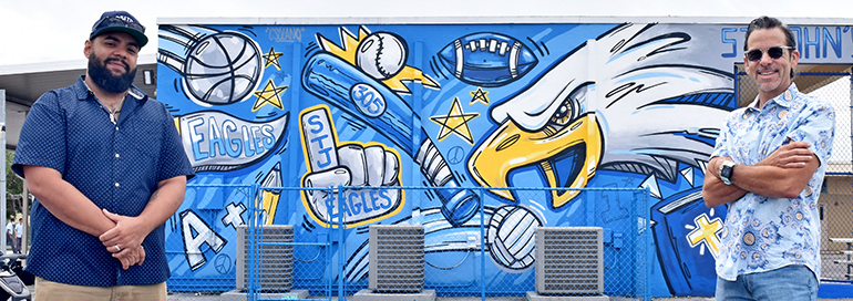 Artist Carlos Solano, left, poses proudly with his mural at St. John the Apostle School, along with alumnus Henry Garcia, whose donation made the mural possible.
