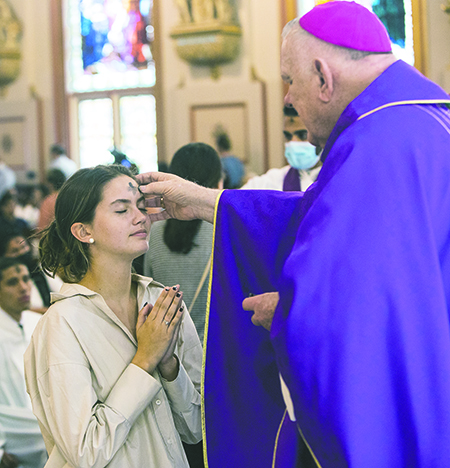 El Arzobispo Thomas Wenski le impone las cenizas a Jade Tate, estudiante de Barry University, durante la Misa que celebr&oacute; el Mi&eacute;rcoles de Ceniza, el 2 de marzo de 2022, en la iglesia Gesu, en Miami.