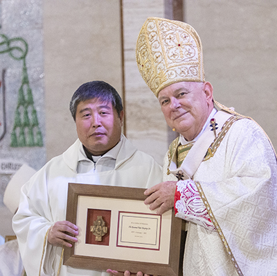 Father Yunping Peter Lin receives a plaque from Archbishop Thomas Wenski commemorating his 25 years of priesthood, April 12, 2022.