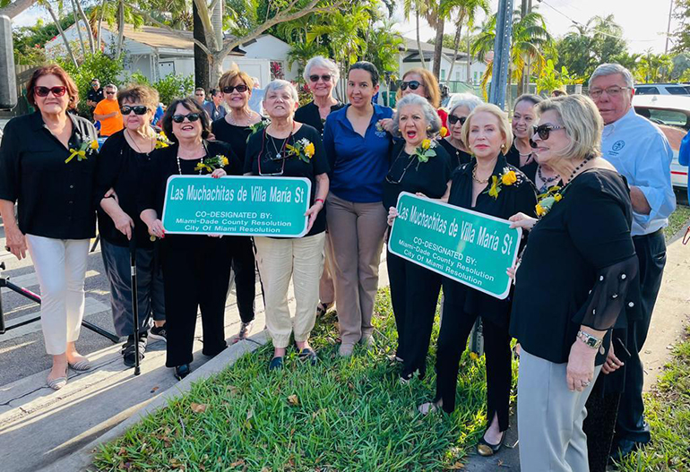 Algunas integrantes del grupo de Las Muchachitas de Villa María posan con el comisionado de la ciudad de Miami, Manolo Reyes, con los letreros donde se muestra la designación de una calle de la ciudad con el nombre de su grupo, el 12 de abril de 2022.