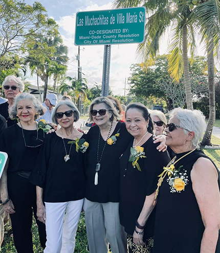 Desde la izquierda, Marilú Cantón, Donaida Lashbrook, Ángela López, Carmen Zamora, Nancy González y atrás Nelly González, integrantes de Las Muchachitas de Villa María, posan con el letrero donde muestra la designación de una calle de la ciudad de Miami con el nombre de su grupo, el 12 de abril de 2022.