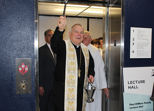 Archbishop Thomas Wenski steps out of an elevator as he blesses with holy water the interior of the new Marcus Lemonis and Mario Sueiras Center for Science and the Arts building at Christopher Columbus High School on April 28, 2022.