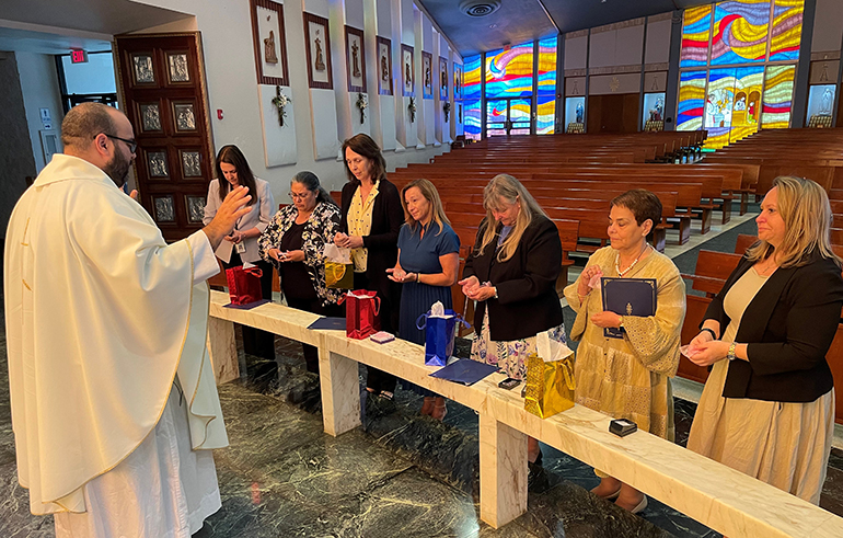Father Matthew Gomez, archdiocesan vocations director, blesses the principals who will be retiring or departing from archdiocesan schools this year; from left: Alex Fernandez of Mary, Help of Christians in Parkland; Annie Seiglie of St. Timothy in Miami; Elena Ortiz of Nativity in Hollywood; Jennifer Nicholson of Annunciation in West Park; Dian Hyatt of St. Lawrence in North Miami Beach; and Carmen Alfonso of St. Michael the Archangel in Miami. Also at far right is Marcey Ayers, who is departing from the archdiocesan Office of Schools.