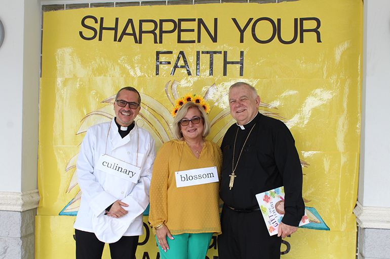 Archbishop of Miami Thomas Wenski poses with Blessed Trinity School's Principal Susy Del Riego and Father Matias Hualpa, administrator of Blessed Trinity Church, in front of one of the posters designed for the Enchanted Book Fair, the week-long literary celebration at Blessed Trinity School that ran from April 25-29, 2022. Archbishop Wenski and Father Hualpa both read to students on April 29.