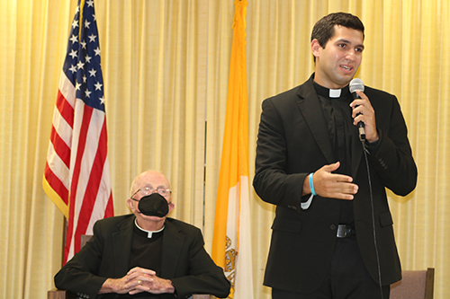 Deacon Gustavo Santos, a seminarian of the Archdiocese of Miami, talks about his journey to the priesthood May 14, 2022, during a Serra Club of Broward County event honoring Father Anthony Mulderry, pastor emeritus of St. Gabriel Parish in Pompano Beach, shown carefully listening to his talk. Father Mulderry is the former chaplain and long-time supporter of the Serra Club of Broward County.