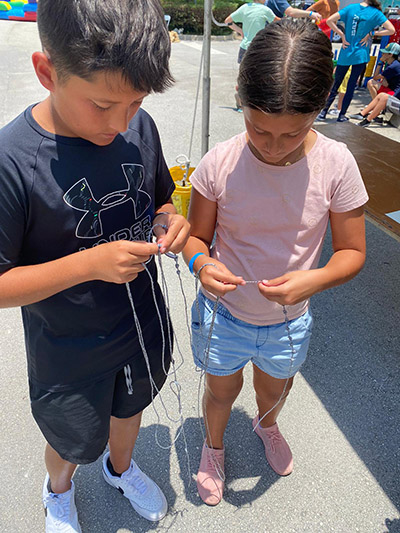 Making rosaries out of string: Ignacio, 13, and Valeria, 11, Dueñas of St. John Neumann Parish, whose grandmother invited them and their mom to the Family Faith Fest, celebrated at Our Lady of Guadalupe, Doral, June 25, 2022.