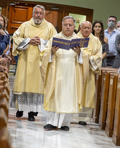 El P. Juan Sosa, párroco de St. Joseph, entra en la iglesia llevando el libro en el que la gente escribió los nombres de las personas por las que rezaban en los días posteriores al derrumbe de Champlain Towers South.