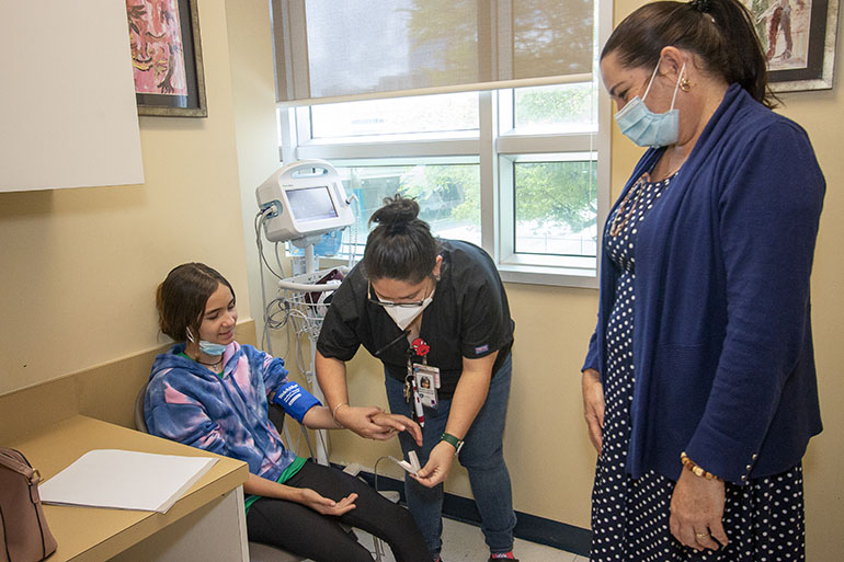 La asistente médica Magally Zelaya le mide la presión arterial a una paciente de 11 años, que llegó de Nicaragua hace tres semanas, mientras su madre la observa, el 29 de julio de 2022, en el Camillus Health Concern de Miami. El personal médico de la clínica proporciona vacunas, exámenes visuales y servicios dentales a niños inmigrantes recién llegados, independientemente de su estatus legal o capacidad económica.