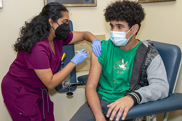 Neha Aitharaju, estudiante de tercer año de Medicina Osteopática de la Universidad Nova Southeastern, vacuna a un paciente de 16 años en Camillus Health Concern de Miami, el 29 de julio de 2022. El personal médico ofrece vacunas, exámenes visuales y servicios dentales a niños inmigrantes recién llegados, independientemente de su estatus legal o capacidad económica.