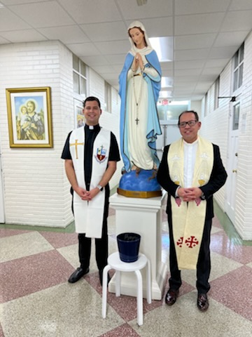 Newly appointed parish administrator Father Luis Flores, right, and newly ordained parochial vicar Father Enzo Rosario Prendes pose next to an image of Mary in an interior hallway at Sts. Peter and Paul School in Miami after blessing it in preparation for the start of the 2022-23 school year.