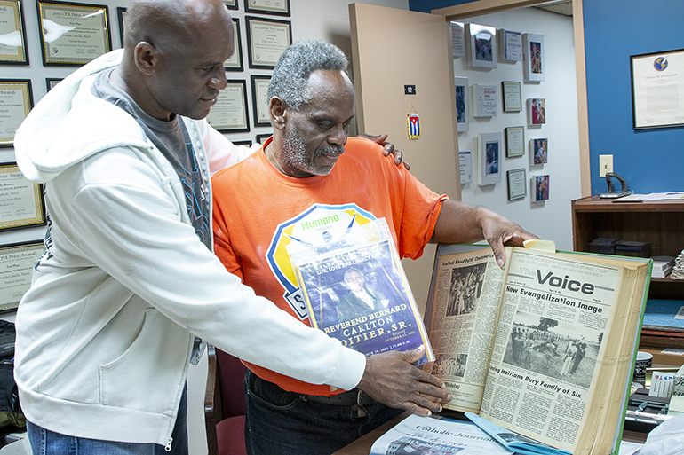Augustin Lorfils, left, and Bernard Poitier look over the coverage of the burial of Lorfils' mother and five siblings in the Aug. 23, 1979 edition of the old archdiocesan newspaper, The Voice. Poitier is holding a memorial of his father, Bernard Poitier Sr., who made him responsible for obtaining a headstone for the family he had buried 43 years ago.
