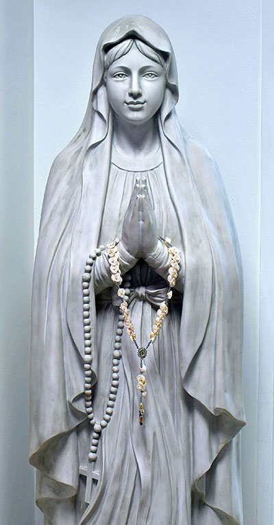A sweet-faced statue of Our Lady of Lourdes greets visitors to St. Boniface Church, Pembroke Pines. She holds a rosary, as St. Bernadette saw her. Someone has also placed another rosary in her hands.