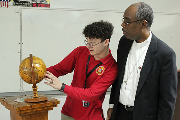 El estudiante de la secundaria Msgr. Edward Pace, Kenneth Martínez busca a Haití en un globo terráqueo junto al Obispo Charles Peters Barthélus de Port-de-Paix, que visitó la escuela de Miami Gardens el 14 de septiembre de 2022.