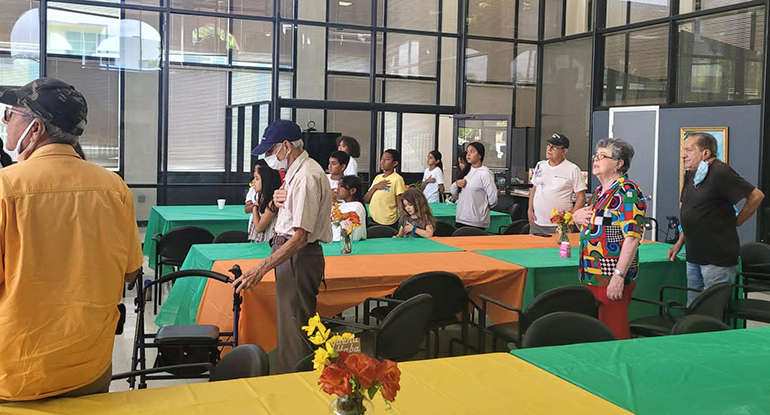 Seniors and youngsters sing the national anthem during a novel intergenerational space-sharing arrangement at a Catholic Charities congregate meal site brought youngsters together with senior citizens during a summer camp experience this year.