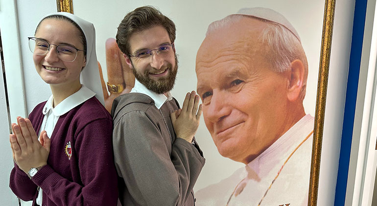 Sister Andrea Isla and Brother Iñigo Johnpaul Isla, siblings who joined the Servants of the Pierced Hearts of Jesus and Mary, pose in front of an image of St. John Paul II outside the studio where the What the Faith, Miami? and Cuéntame Católico podcasts are recorded, Nov. 16, 2022.