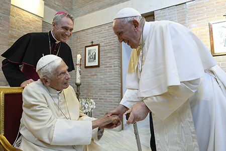 El Papa Francisco saluda al Papa retirado Benedicto XVI en el monasterio Mater Ecclesiae después de un consistorio para la creación de 20 nuevos cardenales en la Basílica de San Pedro, en el Vaticano el 27 de agosto de 2022. El Arzobispo Georg Gänswein, secretario privado del Papa, los observa. (CNS photo/Vatican Media)