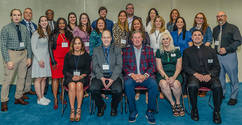 Catholic schools superintendent Jim Rigg, seated second from left, and St. Thomas University president David Armstrong, next to him, pose Jan. 8, 2023 with the 14 archdiocesan educators (standing) who make up the first cohort of students in the master's in educational leadership program for future Catholic school principals. With them are other university officials and the program's professors.