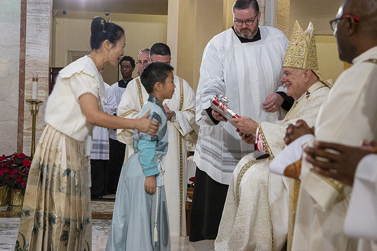 A young member of the Chinese Apostolate takes up a gift for Archbishop Thomas Wenski during the offertory at the annual Migration Mass, Jan. 8, 2023.

Archbishop Thomas Wenski celebrates the annual Migration Mass, welcoming members of the various national and ethnic apostolates in the Archdiocese of Miami, to St. Mary Cathedral on the feast of the Epiphany, Jan. 8, 2022.