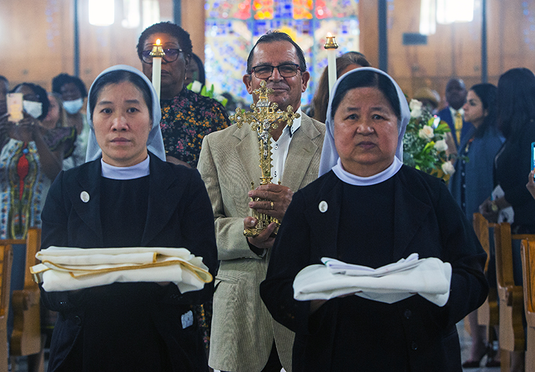 Our Lady of Visitation Sisters Therese Phan, left, St. Helen School religion teacher, and Mother Superior Martha Huong carry the altar cloth as parishioner Jose Arce carries the cross to be placed on the new, and now consecrated, altar of St. Helen Church in Lauderdale Lakes, Jan. 21, 2023.