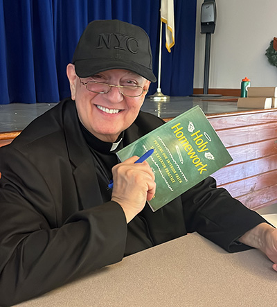Redemptorist Father Robert “Bob” Pagliari holds up a copy of his book, "Holy Homework," while autographing it for students during one of his stops at archdiocesan schools at the beginning of January 2023.
