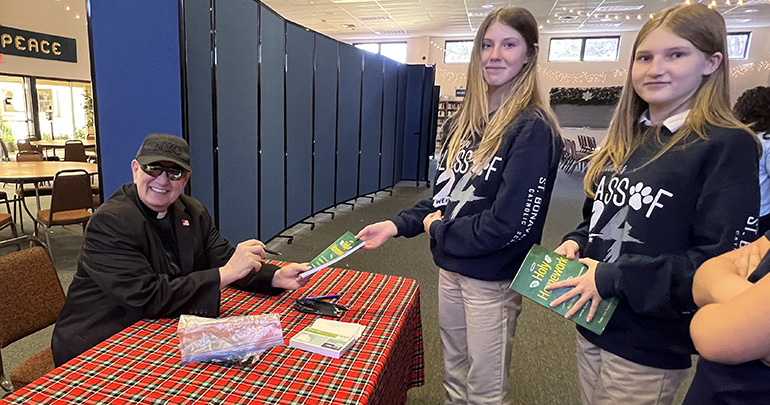 Redemptorist Father Robert “Bob” Pagliari signs copies of his "Holy Homework" book for St. Bonaventure middle school students.