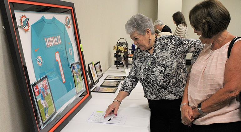 Attendees at the Miami Archdiocesan Council of Catholic Women's annual scholarship luncheon, held Feb. 25, 2023, at the Embassy Suites in Fort Lauderdale, look at items to bid on in a silent auction, like the framed and signed jersey of Tua Tagovailoa, quarterback for the Miami Dolphins football team. All proceeds benefited the MACCW Scholarship Fund for eighth grade girls attending a Catholic elementary school in the Archdiocese of Miami who want to pursue a Catholic education in high school.