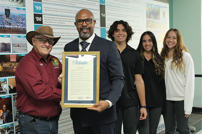 Vice Mayor of Southwest Ranches Jim Allbritton presents a proclamation recognizing April 27, 2023 as Archbishop Edward A. McCarthy High School Day to Principal Richard Jean. Also in the photo are student siblings Christopher, Sophia, and Susanna Inguanzo who worked together to create a 25th anniversary timeline for their school.