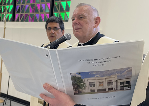 Archbishop Thomas Wenski, with Father Juan Carlos Paguaga, pastor, behind him, reads the blessing prayer at the dedication of the new sports and multipurpose center at St. Agnes Parish in Key Biscayne, May 15, 2023.