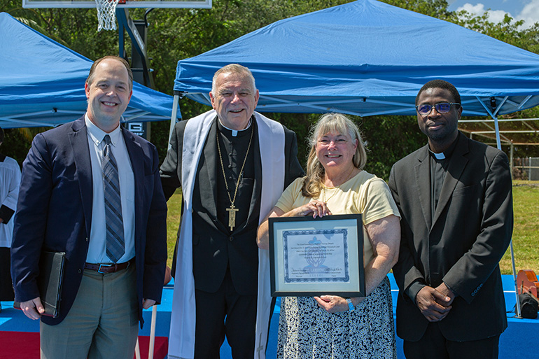 Former St. Lawrence School principal Dian Hyatt holds a plaque noting the dedication of the new basketball-volleyball court in her honor for her 40 years of service to the school, May 16, 2023. Standing alongside, from left: Jim Rigg, archdiocesan schools superintendent; Archbishop Thomas Wenski; and St. Lawrence Church pastor, Father Cletus Omode.