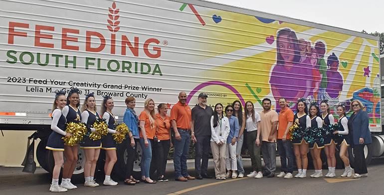 Cheerleaders, staff and faculty of St. Thomas Aquinas High School pose in front of a picture on a truck from Feeding South Florida, created by junior student Leila Murray, and unveiled May 31, 2023, at St. Thomas Aquinas High School, Fort Lauderdale.