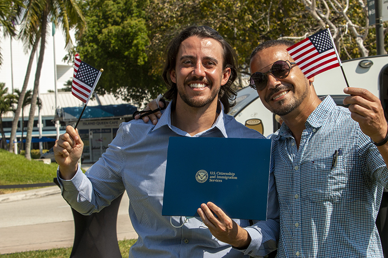 New U.S. citizen Michael Pimenta, left, poses with his naturalization certificate, American flag, and friend Andre Rosa after a citizenship ceremony held in the shadow of the "Angels Unawares" sculpture and Miami's Freedom Tower, March 24, 2021. The Archdiocese of Miami partnered with U.S. Citizenship and Immigration Services to hold the naturalization ceremony there while the sculpture was on display in Miami.