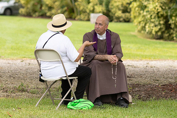 Father Joseph Rogers, who in 2021 who became the first priest to join a new male branch of the Servants of the Pierced Hearts of Jesus and Mary, hears confessions Aug. 5, 2023, before the World Youth Day Miami walking pilgrimage and overnight vigil in Homestead, for young people unable to attend WYD in Lisbon.